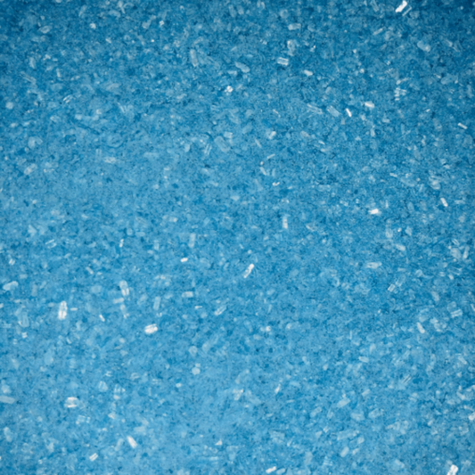 Close-up of fine, bright blue bath soak crystals with a slightly coarse texture and a sparkly, granular appearance