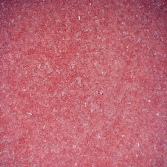 Close-up of fine, light red bath soak crystals with a slightly coarse texture and a sparkly, granular appearance