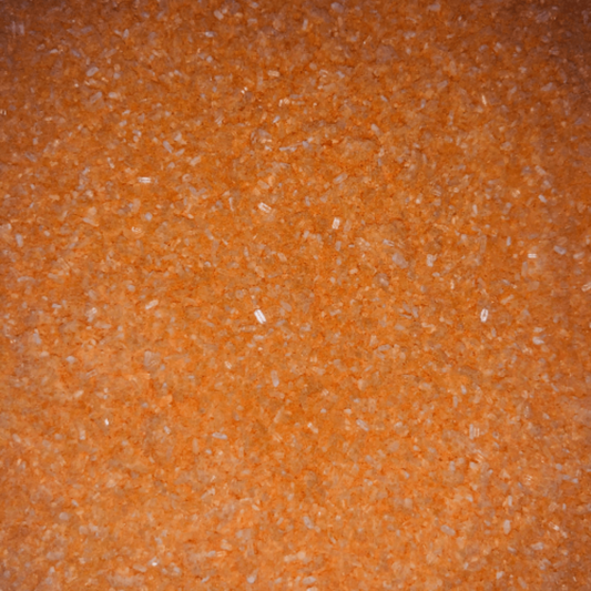 Close-up of fine, bright orange bath soak crystals with a slightly coarse texture and a sparkly, granular appearance