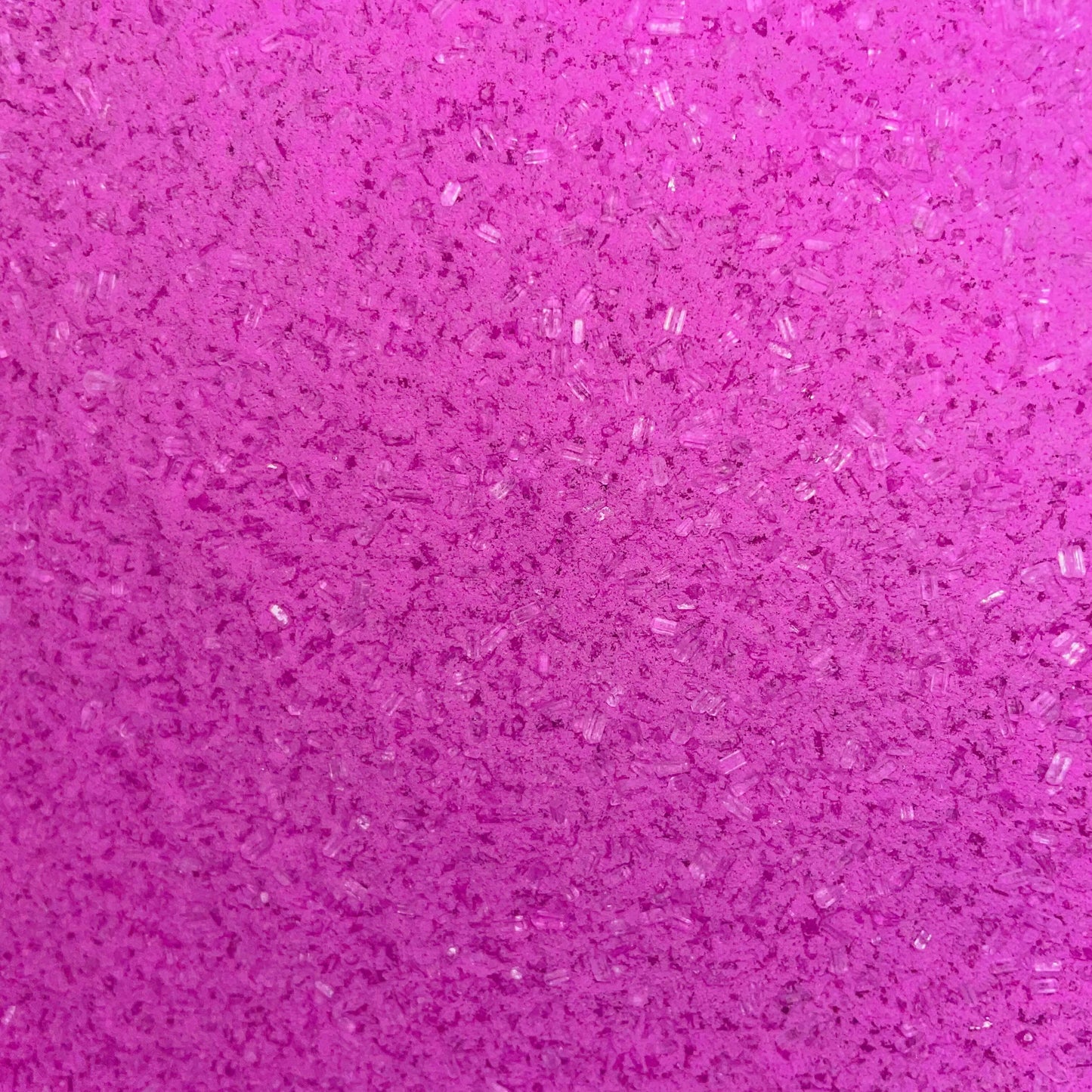 Close-up of fine, bright pink bath soak crystals with a slightly coarse texture and a sparkly, granular appearance
