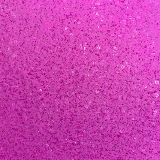 Close-up of fine, bright pink bath soak crystals with a slightly coarse texture and a sparkly, granular appearance