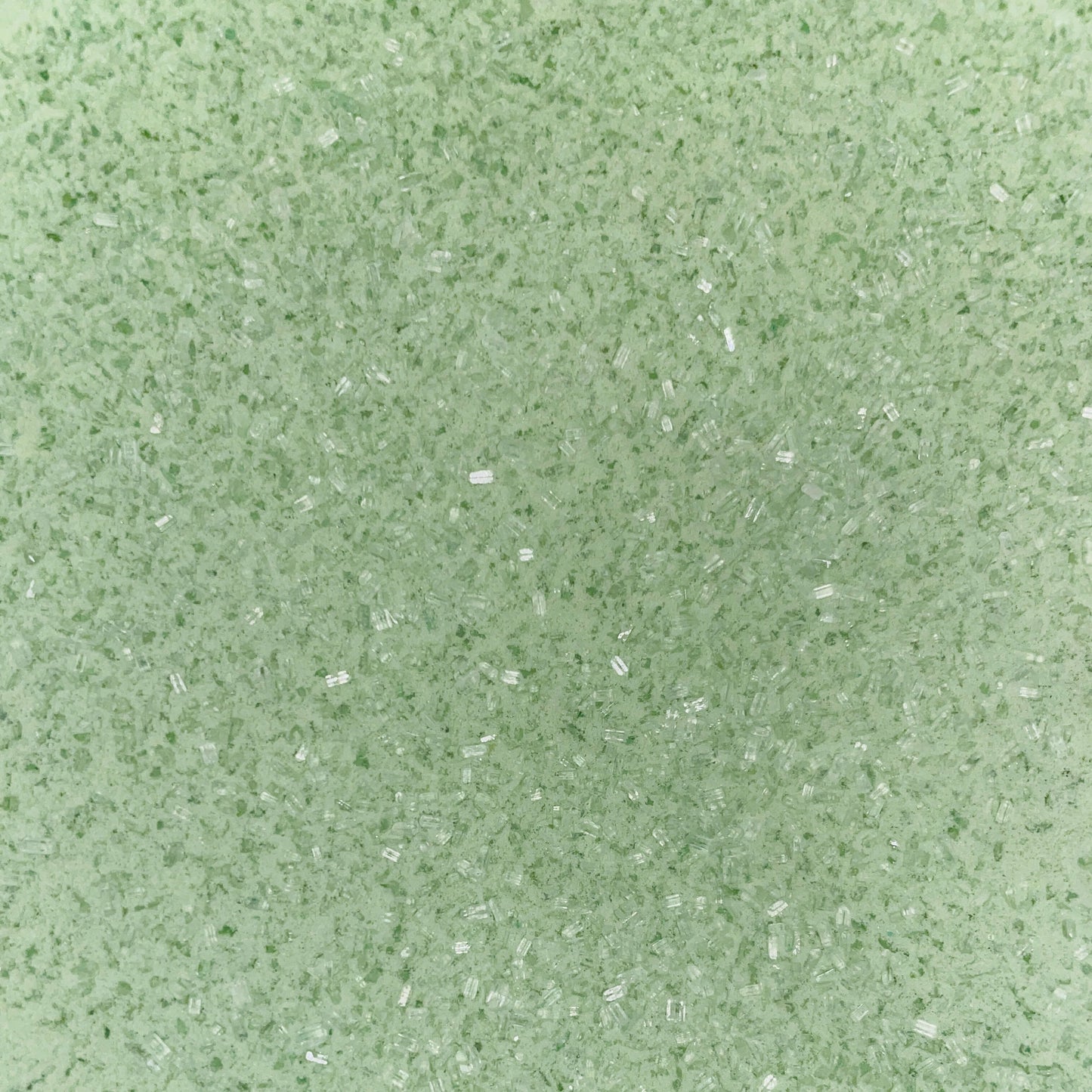 Close-up of fine, light green bath soak crystals with a slightly coarse texture and a sparkly, granular appearance