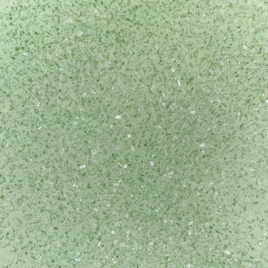 Close-up of fine, light green bath soak crystals with a slightly coarse texture and a sparkly, granular appearance