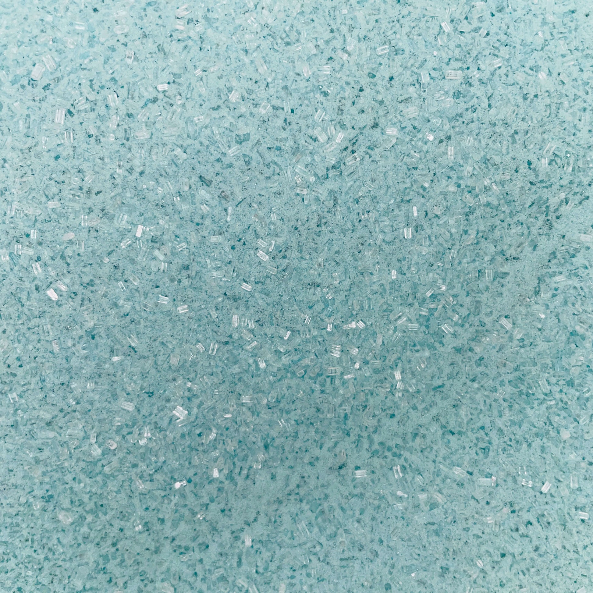 Close-up of fine, light blue bath soak crystals with a slightly coarse texture and a sparkly, granular appearance